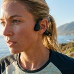 Woman running outdoors wearing open-ear bone conduction headphones.