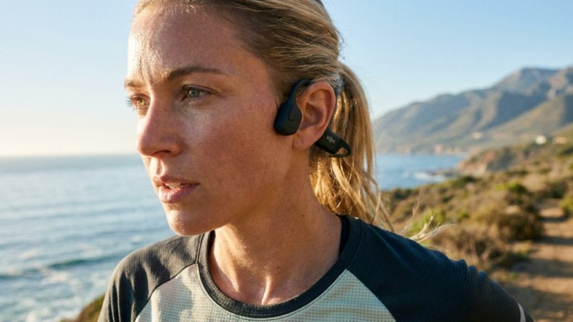 Woman running outdoors wearing open-ear bone conduction headphones.