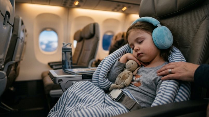 A young boy smiling while wearing blue over-ear headphones on an airplane.