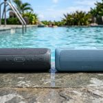 Two waterproof Bluetooth speakers sitting on wet poolside deck for audio comparison.