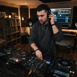 Young male DJ testing closed back audio headphones at a mixing board.