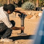 Man installing a heat-resistant solar panel for outdoor holiday lights near desert landscaping.
