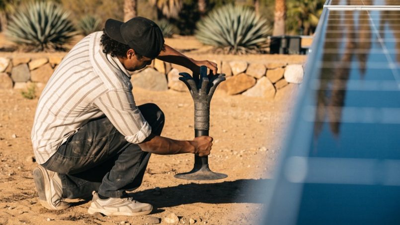 Man installing a heat-resistant solar panel for outdoor holiday lights near desert landscaping.